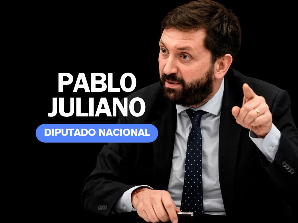 Retrato de un hombre con barba, vestido con un traje negro y una camisa blanca, gesticulando con la mano mientras habla.